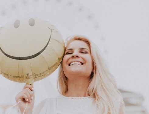 Cheerful woman holding a smiley balloon outdoors on a sunny day, exuding happiness and positivity.